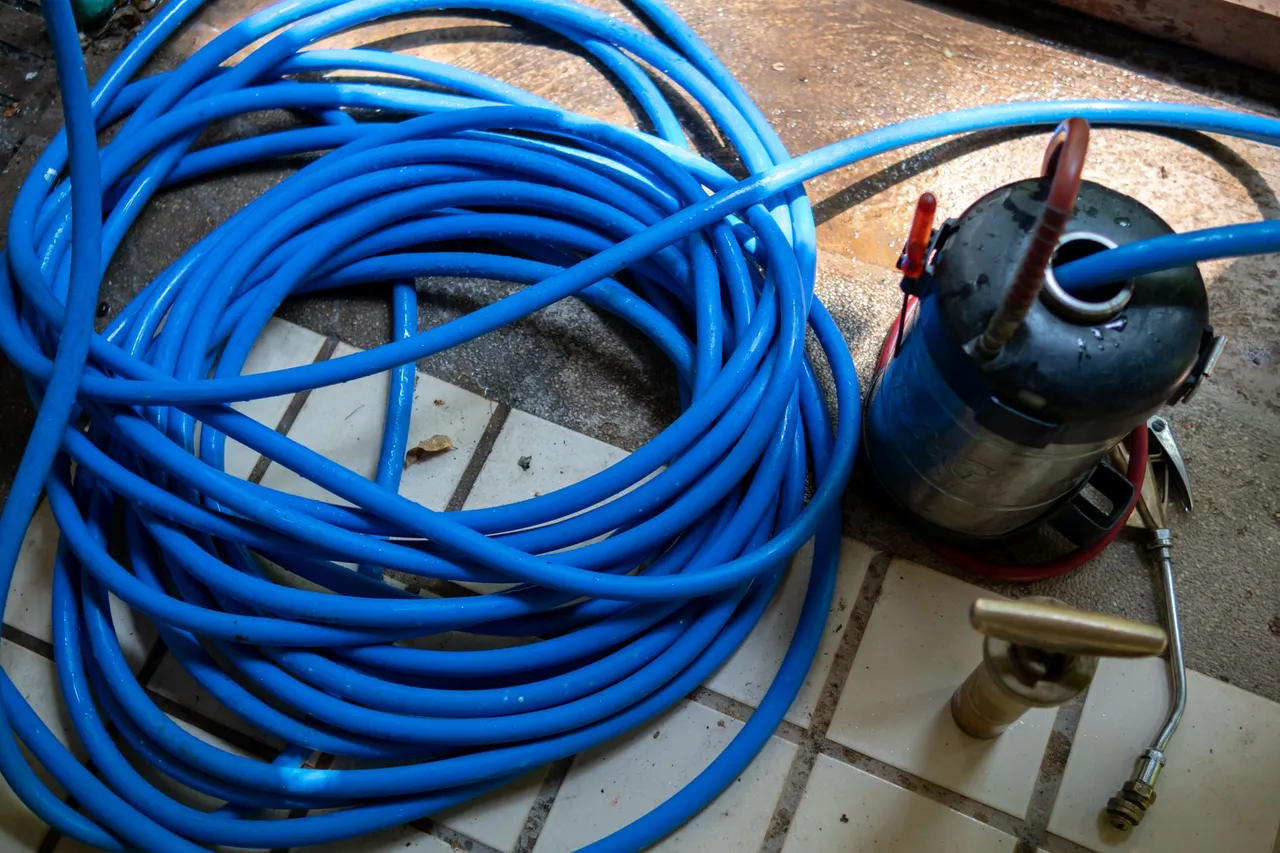 A blue hose is laying on a tiled floor next to a fire extinguisher A blue hose is laying on a tiled floor next to a fire extinguisher
