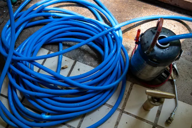 A blue hose is laying on a tiled floor next to a fire extinguisher A blue hose is laying on a tiled floor next to a fire extinguisher